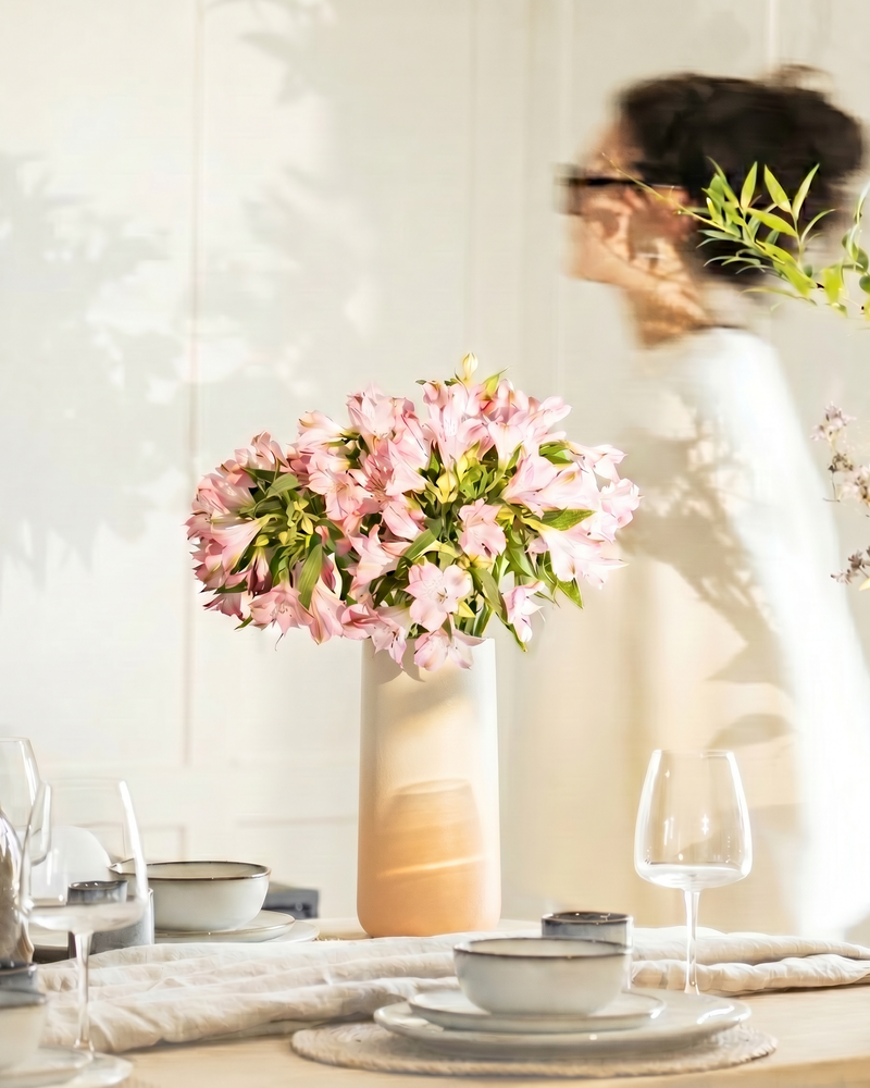 feey Keramik-Vase 'Solio' mit rosa Alstroemerien-Strauß auf einem gedeckten Esstisch, im Hintergrund eine Person