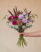 Hand hält den Blumenstrauß Märchenbuch in der Größe Classic mit magentafarbenen Nelken und violetten Blüten