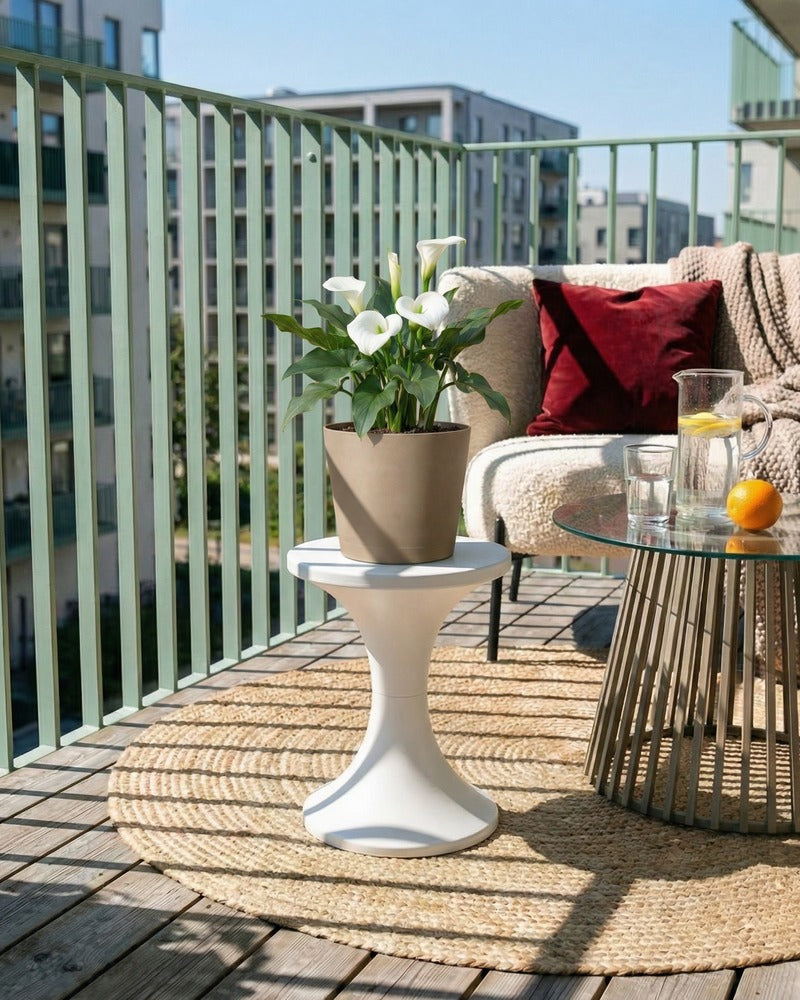 Weiße Calla im beigen Topf auf einem sonnigen Balkon mit Lounge-Sofa