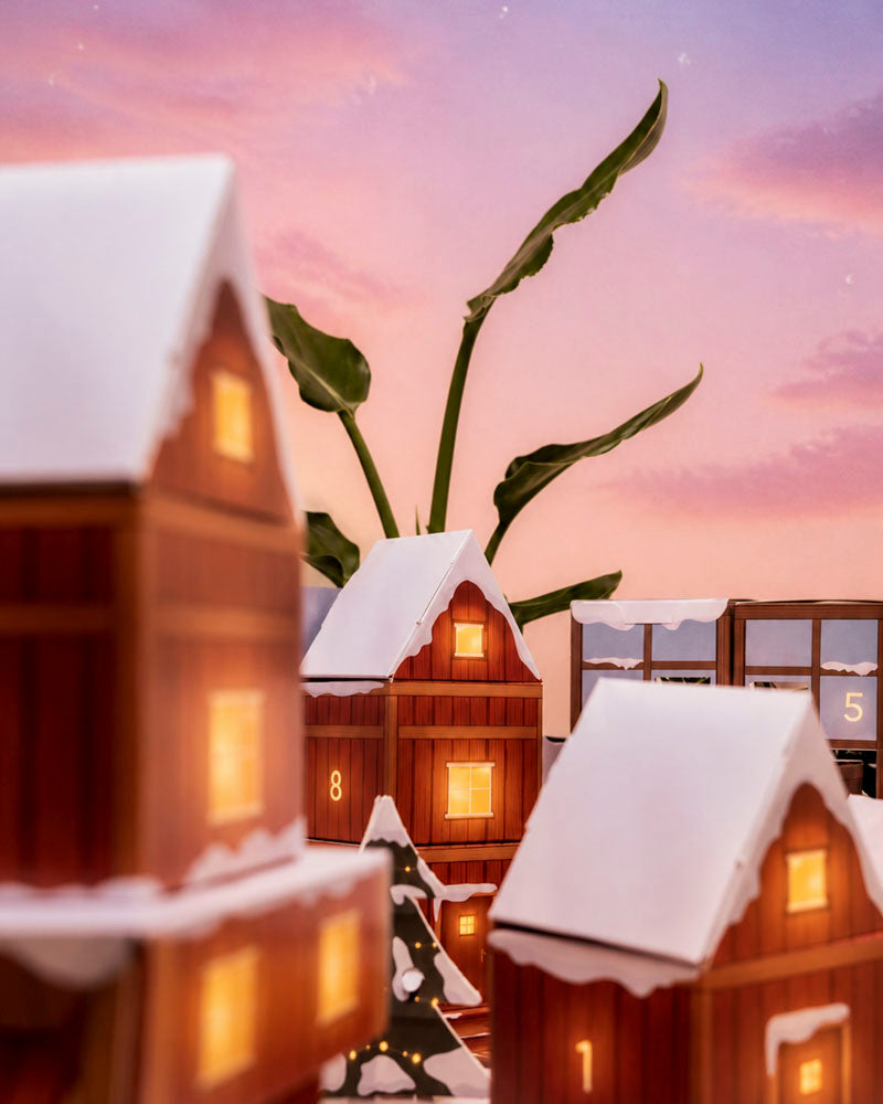 Nahaufnahme der beleuchteten roten Winterdorf-Häuschen mit nummerierten Türchen und kleinem Papier-Tannenbaum vor rosa Morgenhimmel.