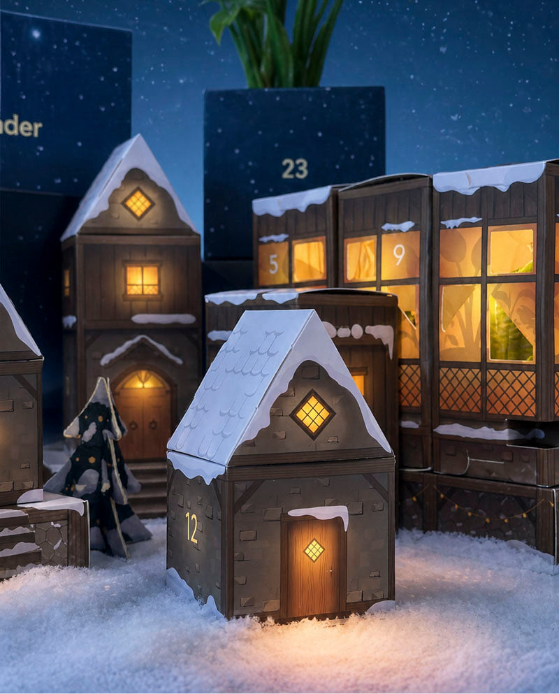 Verschneite, beleuchtete Adventskalender-Häuschen mit nummerierten Türchen vor tiefblauem Sternenhimmel.