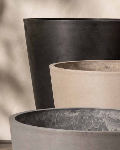 Nahaufnahme von drei minimalistischen, konischen Pflanzkübel-Sets Amsterdam (2x 30) in verschiedenen Farbtönen, von hellbeige bis dunkelgrau. Die glatten Oberflächen und das schlichte Design betonen eine moderne Ästhetik. Die aus Recycling-Kunststoff gefertigten Pflanzkübel verfügen über ein integriertes Drainage-System für optimale Pflanzengesundheit.