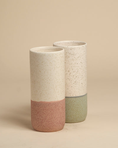 Zwei Keramik-Vasen (Variado | 21 cm), eine mit gesprenkeltem Creme und gedämpftem Rosa, die andere mit Creme und gedämpftem Grün. Ideal als Blumenvase für Zimmerpflanzen, ausgestellt auf einer beigen Oberfläche mit einem passenden Hintergrund.
