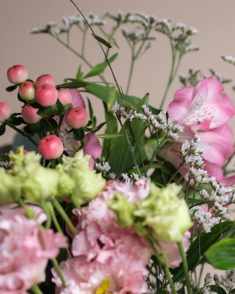 Eine Nahaufnahme des Ballerina-Straußes mit rosa und grünen Blüten, kleinen runden rosa Beeren und zarten weißen Füllblumen vor einem neutralen Hintergrund.