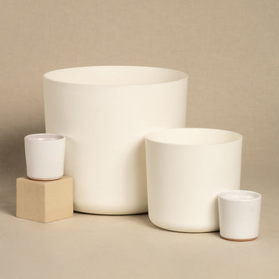Ein Set aus vier minimalistischen weißen Kunststoff-Topfsets „Lumi“ in verschiedenen Größen, wobei zwei kleinere elegant auf einem Holzblock platziert sind. Vor einem neutralen beigen Hintergrund veranschaulichen sie ein schlichtes und modernes Design.