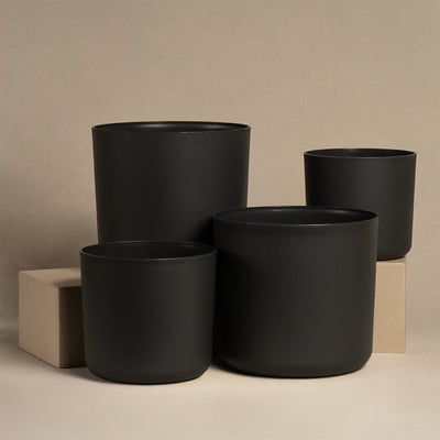 Das Kunststoff Topfset 'Lumi', bestehend aus vier schwarzen Töpfen mit schlichtem Design, wird vor einem neutralen Hintergrund in unterschiedlichen Größen präsentiert. Zwei der Töpfe stehen elegant auf beigen Blöcken.