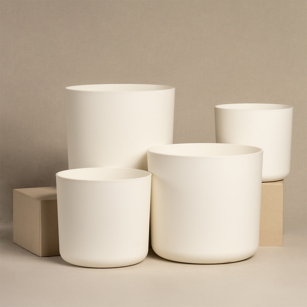 Das Kunststoff-Topfset „Lumi“, bestehend aus zwei cremefarbenen Töpfen im Keramikstil in den Größen 22, 18 und 16, ist auf und neben zwei beigen Boxen vor einem neutralen Hintergrund arrangiert und unterstreicht so das schlichte Design.