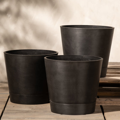 Drei leere schwarze Blumentöpfe unterschiedlicher Größe sind auf einer Holzfläche vor einem neutralen Hintergrund angeordnet. Die schlichten, zylindrischen Töpfe des Pflanzkübel-Sets Venice (3x 30) aus Recycling-Kunststoff werfen im natürlichen Licht subtile Schatten.